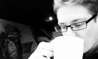 Close-up van een blonde jongeman met bril die en kop koffie drinkt in een cafe